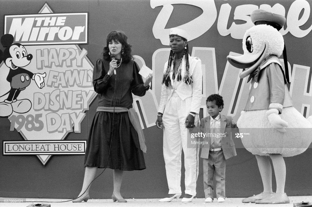 Ghislaine Maxwell standing on stage with a child and Donald Duck at the 1985 Happy Family Disney Day.