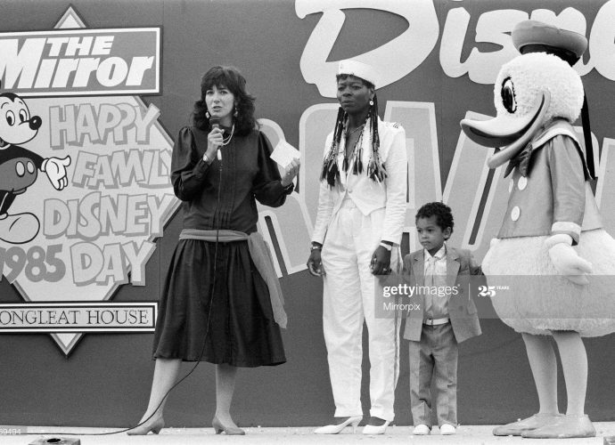 Ghislaine Maxwell standing on stage with a child and Donald Duck at the 1985 Happy Family Disney Day.